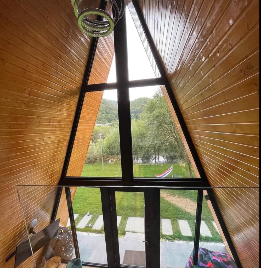 Interior cabană A-Frame — pereți din lemn și fereastră panoramică triunghiulară